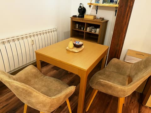 Wooden dining table with two upholstered chairs next to a shelf with cups