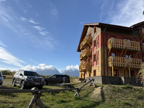 Autá zaparkované na tráve vedľa domu, v pozadí Vysoké Tatry