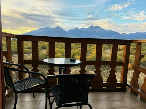 Carved wooden balcony with a round glass table and two chairs facing the High Tatras