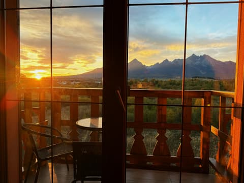 The sun setting beside the High Tatras, seen through the open balcony door with the table and chairs outside