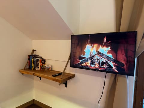 Wall TV next to a rope-hung bookshelf under the sloping ceiling