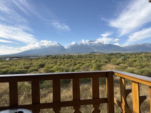 Vysoké Tatry so zasneženými štítmi nad zelenou lúkou z vyrezávaného dreveného balkóna